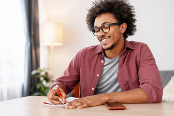 Authentic African American man writer taking notes sitting working at home in modern living room