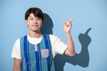 エプロンを着て指差しのポイントポーズをする男性　保育士・介護士などのイメージ　水色背景