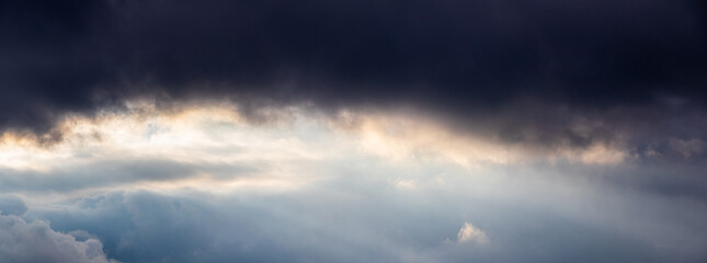 Panoramic view of a dramatic sky with dark storm clouds and a bright ray of light through a gap, symbolizing hope after the storm