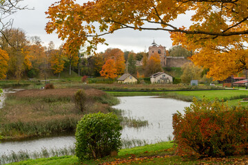Golden autumn leaves frame a tranquil view of Dobele Castle ruins (Latvia) and nearby houses...
