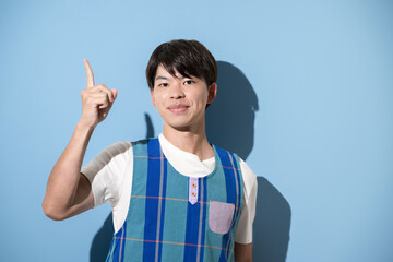 エプロンを着て指差しのポイントポーズをする男性　保育士・介護士などのイメージ　水色背景