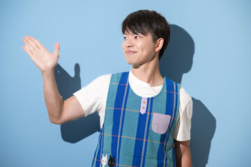エプロンを着てオススメや紹介のポーズをする男性　保育士・介護士などのイメージ　水色背景