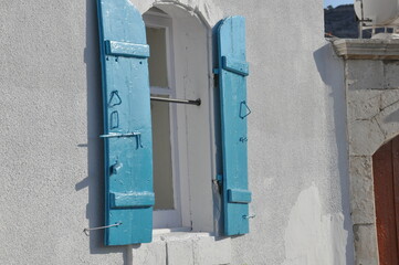 Shuttered window with blue shutters in a coastal village under bright sunlight