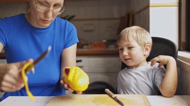 Mother peeling mango fruit for her son in the kitchen