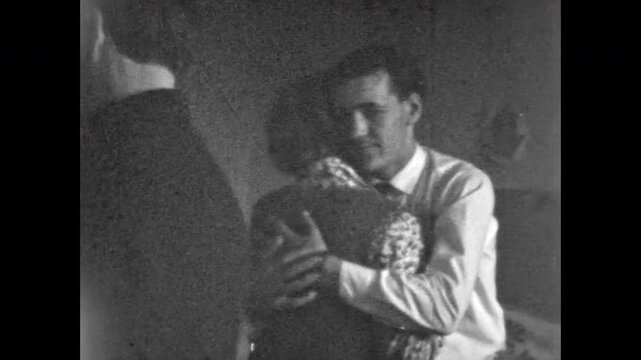 Young couple dance in room, man and woman glide in slow romantic steps, smiling faces, joyful intimacy and connection, soft warmth, playful gesture. Old film. Archival retro 1960s. Vintage archive.