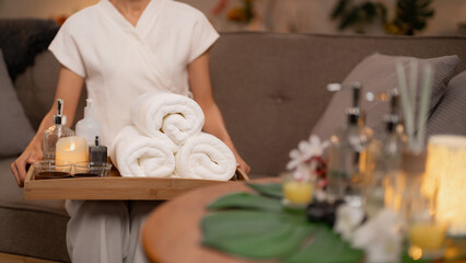 Asian Adult Woman Spa Therapist Holds Wellness Treatment Tray With Rolled Towels Oils Candle Providing Serene Relaxation Service In Luxury Spa Setting