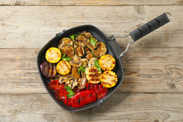 Delicious grilled vegetables, mushrooms and parsley in pan on wooden table, top view