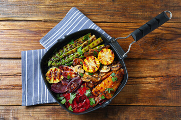 Delicious grilled vegetables, mushrooms and spices in pan on wooden table, top view