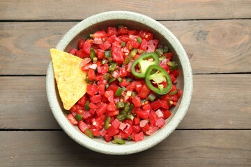 Tasty salsa with nacho chip on wooden table, top view