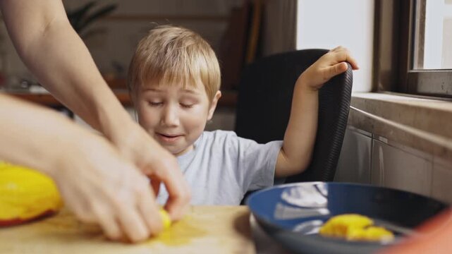 Mother preparing fresh mango fruit for her little son in the kitchen