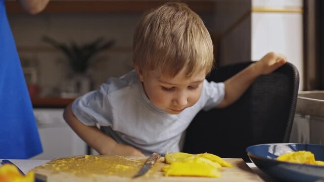 Curious little boy eating juicy mango slices