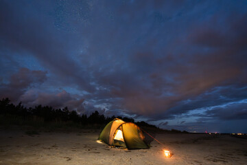A solitary illuminated tent glows warmly on a deserted sandy beach in Estonia during a peaceful night of wild camping.