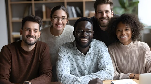 Diverse group of young professionals gather, smiling brightly, for a team portrait in modern office setting.