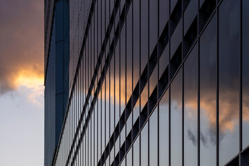 Modern corporate building facade with dark glass panels reflecting sunset clouds emphasizing transparency, precision, and corporate atmosphere of economic stability