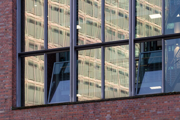 Modern glass architecture with reflections of urban buildings on red brick base façade under soft afternoon light conveying transparency, geometry, and corporate identity