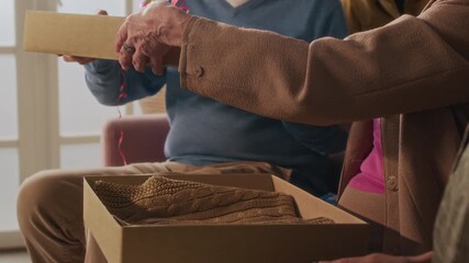 Tilt up view of smiling birthday lady opening cardboard box and taking brown vest out, she trying it on showing present to friends at festive party