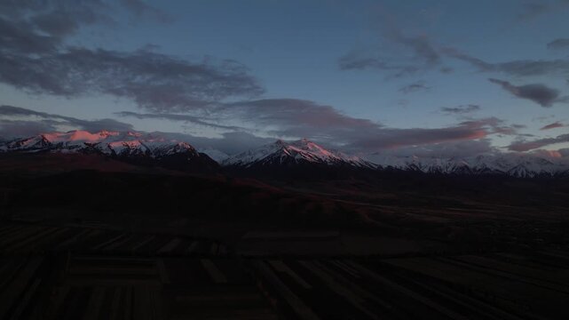 Stunning Dusk Over Majestic Snow-Capped Mountains Surrounded by Expansive Fields and Dramatic Clouds, Captured in Serene Twilight Atmosphere.