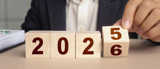2025 transition: A person hand switches the number from 2025 to 2026. This action symbolizes the forward movement of a business year to a new chapter.