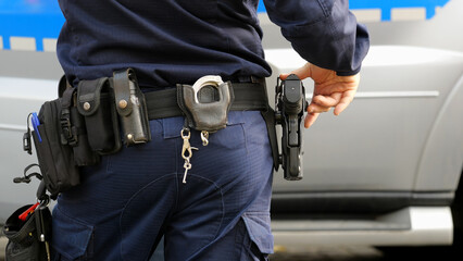 Police officer in a uniform with his hand on holstered pistol, duty belt carrying handcuffs, pepper...