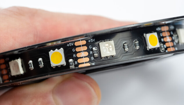RGBW LED strip macro detail closeup with 5V solder pads and cut line mark, flexible SMD light tape held in hand, addressable RGB plus white channels on black PCB for diy smart home color backlight