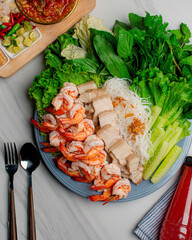 Shrimp and pork belly served with fresh vegetables and delicious dipping sauce, served as a set on a white table.