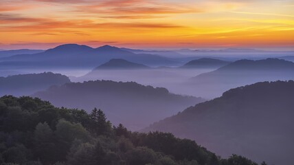 A scenic view of mountain ranges covered in mist under a vibrant orange and yellow sunrise sky landscape