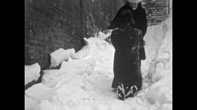 Proposes marriage in winter snowy street. Young man kneels in snow to girlfriend in city. Romantic couple relationship in cold outdoor. Vintage love film. Old archive. Archival retro 1960s proposal