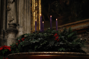 A beautifully arranged advent wreath adorned with evergreen foliage and vibrant candles, softly illuminated by candlelight in a serene church interior