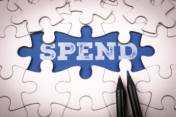 Word spend written on blue background under white puzzle pieces symbolizing finance budgeting money management and investment planning concept