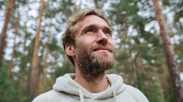 Man in forest, standing near pine trees, looking at camera.