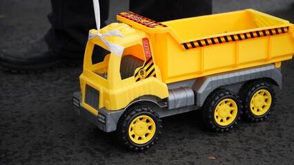 Bandung, October 17, 2025: Close-up of a yellow plastic dump truck toy on a black asphalt road, perfect for concepts of childhood, playtime, or construction toys.