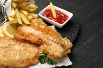 British Traditional Fish and chips with sauce and lemon on dark textured table, closeup