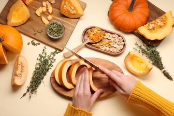 Woman cutting pumpkin on beige background, above view