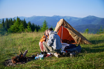 Scenic mountain campsite with two tents in morning. Two campers enjoying serene view of rolling...
