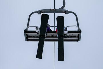 Two snowboarders on chairlift climb mountain