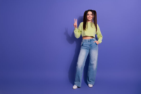 Fototapeta Playful young woman in casual outfit posing on colorful violet background with cheerful peace hand gesture
