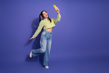 Happy young woman in casual outfit posing for a selfie against a purple backdrop with vibrant...