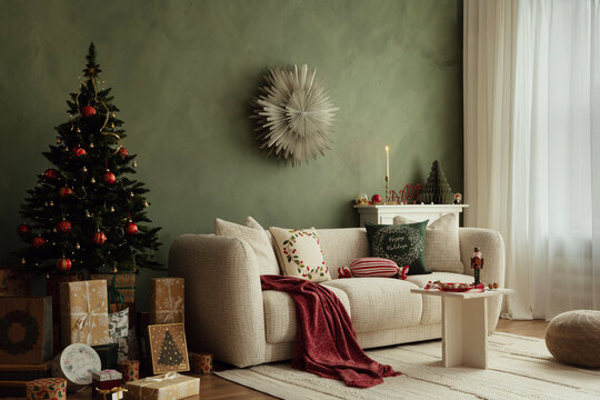 Christmas living room with decorated tree and presents under it. Cozy beige sofa, red throw blanket, and stylish holiday cushions.