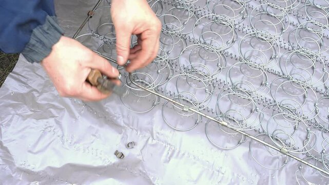 A person is repairing a metal bed frame in a workshop. The individual uses tools to tighten components while surrounded by a clean, organized workspace in daylight