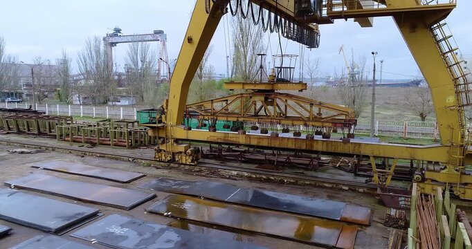 Gantry crane lifting steel sheets with electromagnet in metal warehouse. Storage of metal sheets in outdoor warehouse. Steel Sheets Warehouse. Sheet Metal. Lifting Equipment,