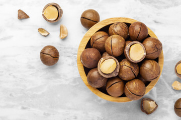 Macadamia nuts with shell in wood bowl and cracked macadamia on marble table background