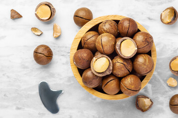 Macadamia nuts in wooden bowl with cracked macadamia  and tool on marble table, close up