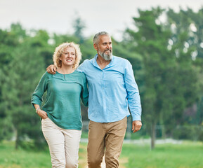 Happy active middle aged white couple having fun walking holding hands and bonding in park outdoors