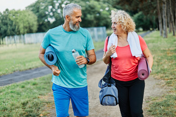 Happy active middle aged couple having fun talking and bonding after having a yoga pilates exercise in park outdoors
