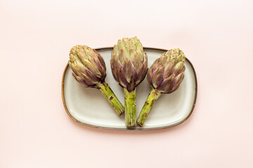 Tree heads of purple artichokes on a plate top view. Vegetables food ready to cook