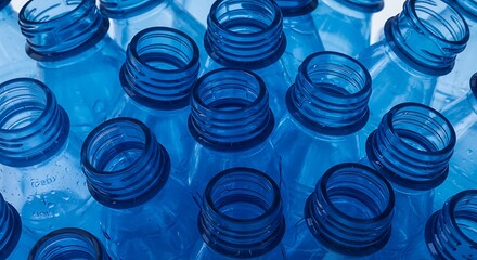 Close up of numerous clear plastic bottle openings against a blue background