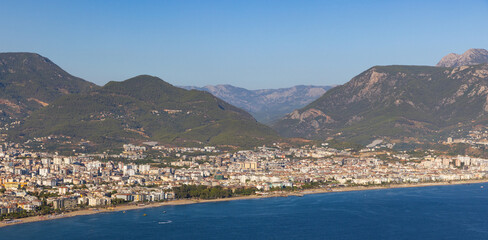 Naklejka premium A broad view of a seaside city built along the shore, set against green mountains