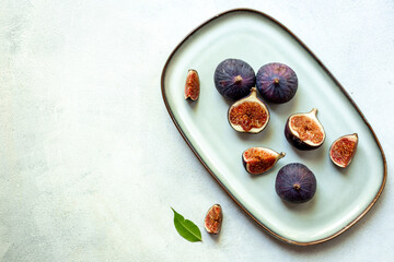 Purple ripe figs and slices with leaves on a plate top view on a stone background