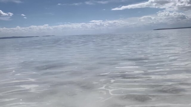 Normal shot video of a salt lake with slightly rippling water caused by gentle wind, under a partly cloudy sky