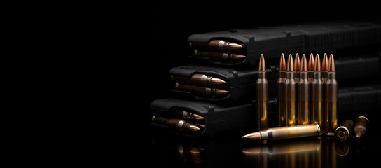 A stack of rifle magazines and 5.56/.223 caliber ammunition on a reflective black back